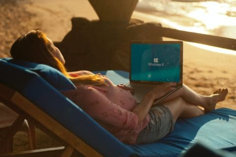 a woman lounging in a beach chair holding a laptop, getting ready to do remote work outdoors