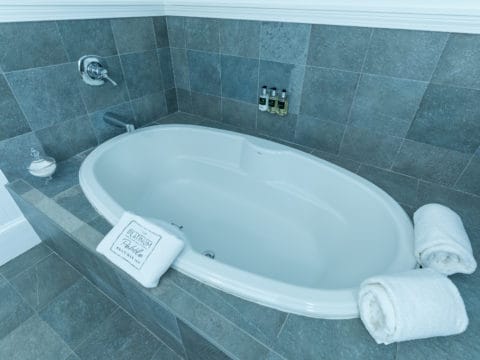 White oval tub surrounded by grey tiles and white towels.