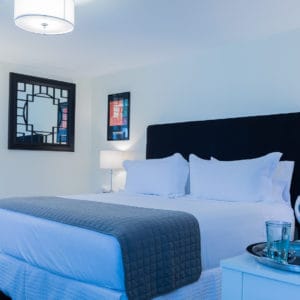 Bedroom with off white walls and black accented chairs, headboard and photos and a grey bed saddle on a white bed