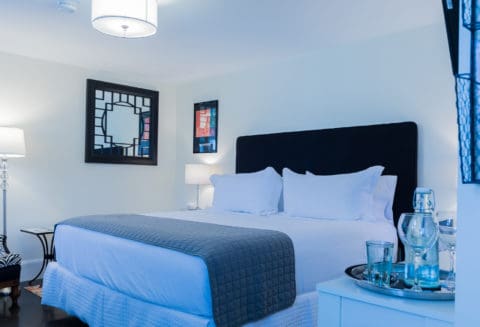Bedroom with off white walls and black accented chairs, headboard and photos and a grey bed saddle on a white bed