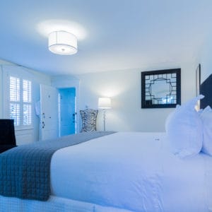 Bedroom with off white walls and black accented chairs, headboard and photos and a grey bed saddle on a white bed