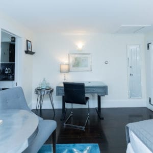 White bedroom with blue accents. A desk and chair with a small side table and a full length mirror on the wall