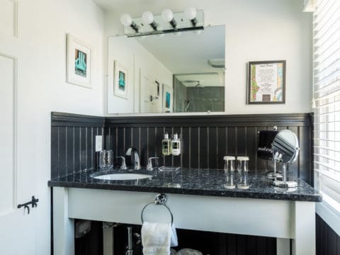 bathroom vanity with black granite top, black wainscoting, mirror with lights above it and 2 pictures on the wall.