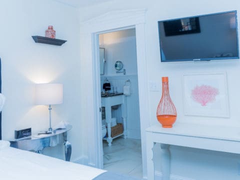 bedroom in white with orange accents, a tv on the wall and looking into the bathroom