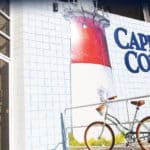 a photo of the cape cod chips factory depicting a lighthouse in red and white and a bicycle leaning against a white pipe railing