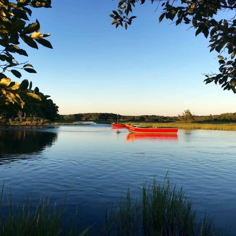 a painted red wooden row boat in the river in Harwich