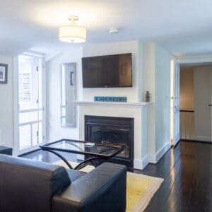 Room with black leather sofa, black and glass coffee table in front of a gas fireplace with a tv above it.