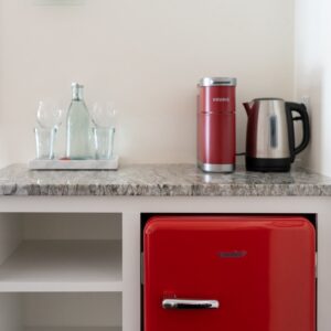 A dry bar with a red retro fridge, coffee bop and glass bottle of water with 2 glasses.
