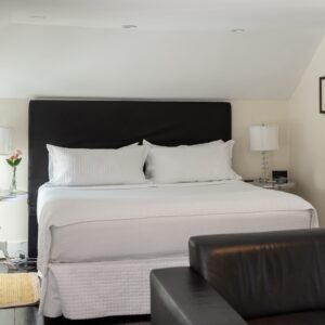A white bedroom with black headboard and yellow accents. silver end tables with lamps, black leather sofa in the forground