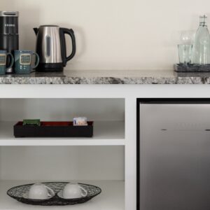 Dry bar showing a silver fridge, coffee pot nd mugs and bottle of water and glasses