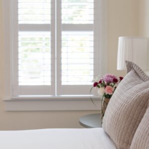 White bedroom with taupe accents. Silver bed side table with lamp and vase of flowers