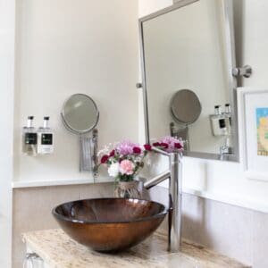 Bathroom with a brown bowl sink, mirror above and a vase of flowers to the side