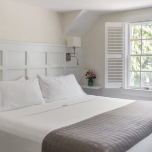 Bedroom in white with a light grey bed saddle. White plantation shutters, custom white headboard and 2 wall mounted lights.