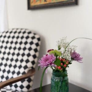 black and white houndstooth chair with a small black side table holding a green vase of flowers. A picture is on the wall above the chair