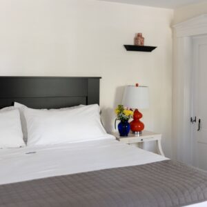 Off white walls of a bedroom with a black headboard and white and grey bed clothes. Orange accents throughout the room.