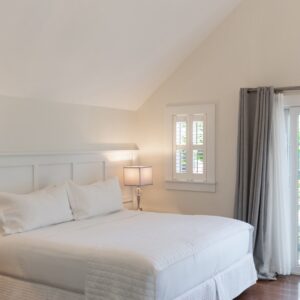 A white bedroom with french doors and grey curtains. Side tables with lamps