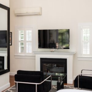 A room showing 2 black chairs, a tv above a gas fireplace, 2 windows and a full length mirror
