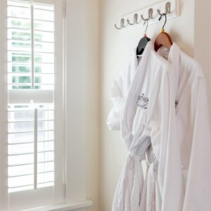 Two robes hanging on the wall beside a window with plantation shutters