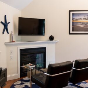 Gas fireplace and two black leather chairs. A tv is on the wall as well as a pictures and large blue starfish