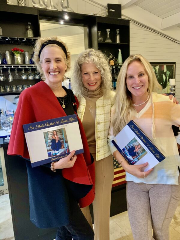 Three blond women are smiling and two are holding a book