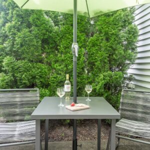 A table, chairs and umbrella on a patio next to a building with trees behind the table.