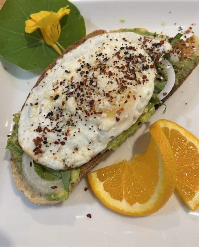 Fried egg on avocado toast with nasturtium leaves and flowers and an orange twist